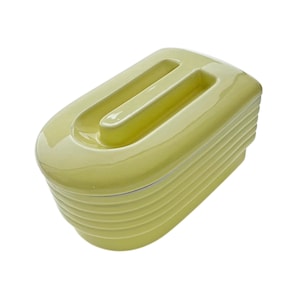 May include: A rectangular ceramic butter dish with a glossy light yellow finish. The lid features a raised, elongated handle centered on top, while the base and lid are designed with horizontal ribbed detailing along the sides for a textured appearance.