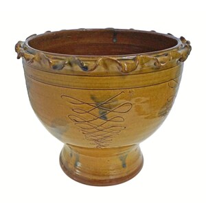 May include: A brown ceramic bowl with a ruffled rim and a decorative design. The bowl has a wide base and a narrow opening.