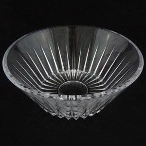 May include: A clear, cut-glass bowl with a wide, flared rim and a circular base. The bowl features vertical, linear cuts radiating from the base to the rim, creating a starburst effect. The bowl is transparent, allowing light to pass through.