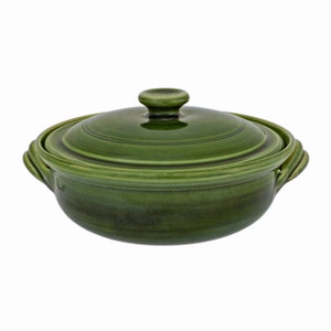 May include: A green ceramic casserole dish with a lid. The dish has a round shape with a handle on each side. The lid has a small knob on top. The dish is a solid, dark green color.