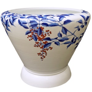 May include: A white ceramic planter with a blue and red floral design. The planter has a wide opening and a narrow base.