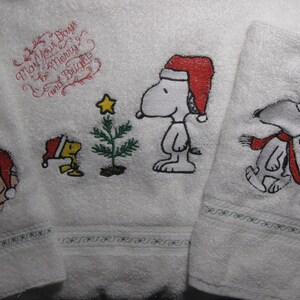 May include: Set of three white towels with embroidered Christmas designs featuring Snoopy and Woodstock. The towels have the text "May Your Days Be Merry and Bright".