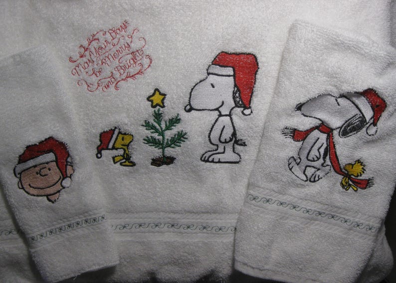 May include: Set of three white towels with embroidered Christmas designs featuring Snoopy and Woodstock. The towels have the text "May Your Days Be Merry and Bright".