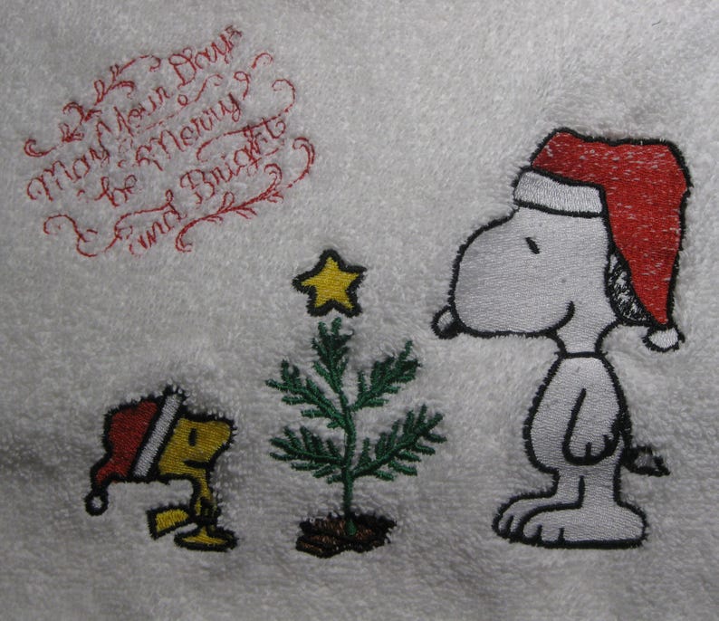 May include: Embroidered design featuring Snoopy wearing a red Santa hat, standing next to a small Christmas tree with a yellow star on top. A small yellow bird with a red Santa hat is to the left of the tree. The text "May Your Days Be Merry & Bright" is embroidered in red cursive at the top of the image.