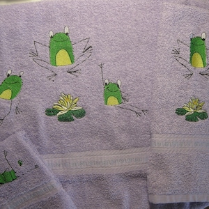 May include: Purple bath towels with embroidered green frogs and lily pads. The towels have a decorative border.