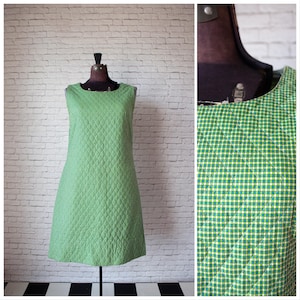 May include: A sleeveless, green and white checkered dress with a quilted pattern. The dress is displayed on a mannequin against a white brick wall. The dress has a round neckline and a straight silhouette.