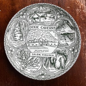 May include: A decorative plate with a black and white illustration of Dixie Caverns in Salem, Virginia. The plate features images of the caverns and surrounding areas, including the Chapel Room and the Wedding Bell.
