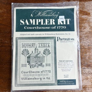May include: A Williamsburg Sampler Kit featuring the Courthouse of 1770, designed by Paragon Needlecraft. The kit includes stamped sampler on Belgian linen, embroidery thread, and instructions. The image shows a cross-stitch design of a building, trees, and text.