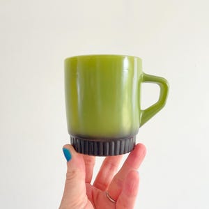Puede incluir: Una taza de cerámica blanca con asa negra y el texto "But First, Coffee" en negrita negra. La taza se encuentra sobre un fondo neutro, resaltando su diseño sencillo.