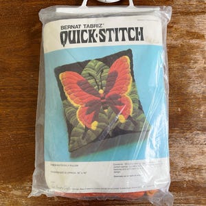 May include: A Bernat Tabriz Quick Stitch butterfly pillow kit in a clear plastic package. The packaging features a graphic of a red and orange butterfly on green leaves, with the text Bernat Tabriz Quick Stitch and finished size 16 inches by 16 inches.