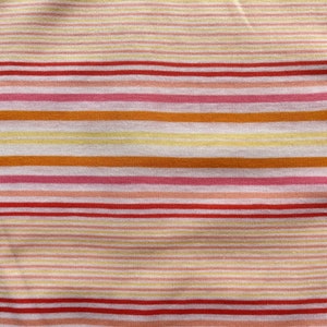 May include: Close-up of a fabric with horizontal stripes in shades of red, pink, orange, and yellow. The stripes vary in width and create a colorful, textured pattern. The fabric appears to be soft and lightweight.
