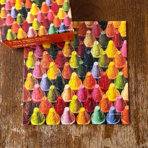 Pode incluir: Um mini quebra-cabeça Springbok com um padrão colorido de pontas de giz de cera em vários tons de vermelho, amarelo, verde, azul e roxo. A tampa da caixa exibe a mesma imagem e texto indicando que é um quebra-cabeça com mais de 70 peças.