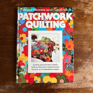 May include: A hardcover book titled Better Homes and Gardens Patchwork & Quilting. The cover features a vibrant, multi-colored floral pattern with a central inset photograph of a quilt. The text includes Quilting, Patchwork, Appliqué basics.