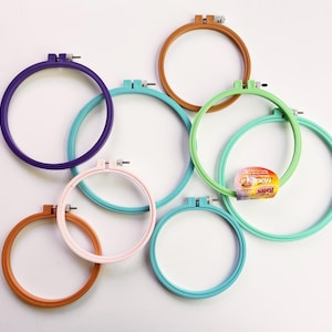 May include: A set of seven embroidery hoops in various colors, including purple, pink, green, and brown. The hoops are made of plastic and have a screw-on closure.