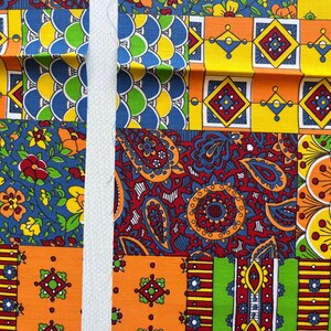 May include: A vibrant patchwork fabric featuring a variety of colourful patterns including geometric shapes, floral motifs, paisley designs, and scalloped scales in shades of yellow, orange, red, blue, and green, bisected by a vertical white fabric strip.