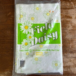 May include: A packaged white table cover with a daisy pattern. The cover is approximately 54 inches by 104 inches. The packaging has the words "Field Daisy" in a green rectangle.