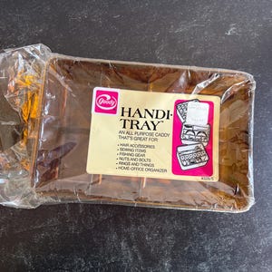 May include: A rectangular, amber-colored plastic Handi-Tray organizer in its original clear plastic packaging. The label features the Goody logo, the text Handi-Tray, and a list of uses including hair accessories, sewing items, and fishing gear.