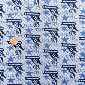 May include: Light blue fabric with a repeating pattern of navy blue cannons, stars, and the number "1776". The fabric has a textured appearance, with a small coin for scale.