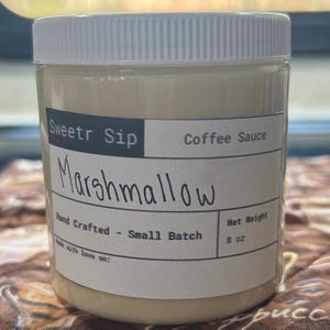 May include: A white jar with a black and white label that reads "Sweetr Sip Coffee Sauce Marshmallow Hand Crafted - Small Batch Net Weight 8 oz".