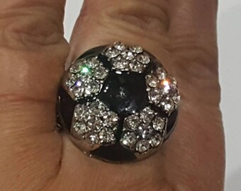 May include: A black and white ring with a soccer ball design. The ring is covered in clear rhinestones.