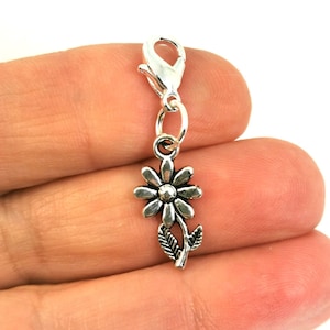 Peut inclure: Breloque en argent avec un motif de marguerite. Le breloque a un fermoir à ressort pour l'attacher à un bracelet ou un collier.