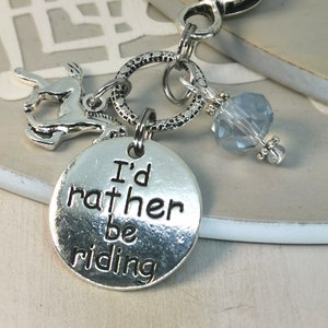 Puede incluir: Encanto de plata con un caballo, un corazón, un cristal y un encanto redondo que dice "Prefiero estar montando".