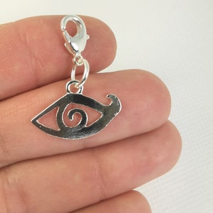 May include: Silver charm featuring a detailed eye design. The eye has a spiral inside and is attached to a silver lobster clasp.