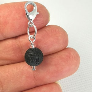 May include: A silver charm with a black lava rock bead and a silver lobster clasp.