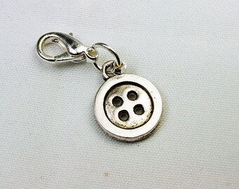 Pode incluir: Um charm prateado com design de botão e quatro furos, preso a um fecho de lagosta. Perfeito para joias ou projetos de artesanato. O charm de botão redondo tem uma aparência ligeiramente envelhecida.