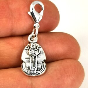May include: Silver charm featuring a detailed depiction of an Egyptian pharaoh's sarcophagus. The charm has a lobster clasp for attaching to a bracelet or necklace.