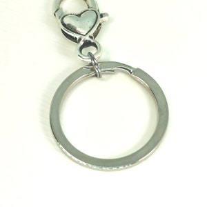 May include: A silver key chain with a heart-shaped clasp and a round ring.
