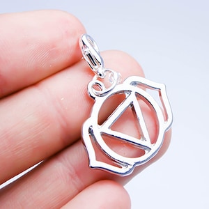 Pode incluir: Pingente de prata com o símbolo do chakra Ajna, também conhecido como o terceiro olho. O símbolo é uma flor de lótus estilizada com um triângulo dentro.