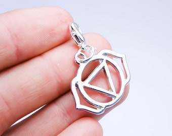 May include: Silver charm pendant featuring the Ajna chakra symbol, also known as the third eye chakra. The symbol is a stylized lotus flower with a triangle inside.