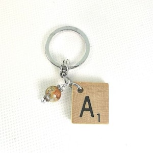 May include: A silver key chain with a brown wooden tile that says "A1" and a small, multi-coloured stone bead.