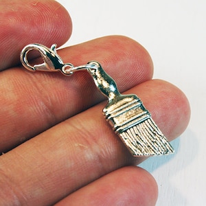 May include: Silver paintbrush charm with a lobster clasp. The charm is in the shape of a paintbrush with a silver handle and bristles.