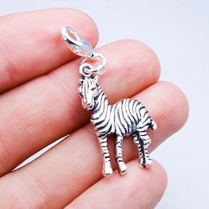 Op de afbeelding: Een zilveren bedel in de vorm van een zebra. De bedel heeft een gedetailleerd ontwerp en is bevestigd aan een zilveren springring.