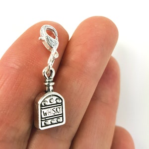 May include: Silver charm in the shape of a whisky bottle with the word "WHISKY" on the front. The charm has a lobster clasp.