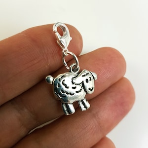 Op de afbeelding: Zilveren bedel met een schattig cartoon-schaapontwerp. De bedel heeft een kreeftclip om aan een armband of ketting te bevestigen.