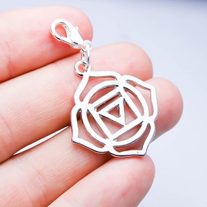 Op de afbeelding: Zilveren bedel met een gedetailleerd ontwerp van een chakra-symbool, in de vorm van een bloem met een driehoek in het midden. De bedel heeft een karabijnhaak om aan een ketting of armband te bevestigen.