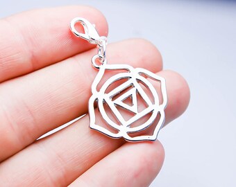 May include: Silver charm with a detailed design of a chakra symbol, featuring a flower-like shape with a triangle in the center. The charm has a lobster clasp for attaching to a necklace or bracelet.