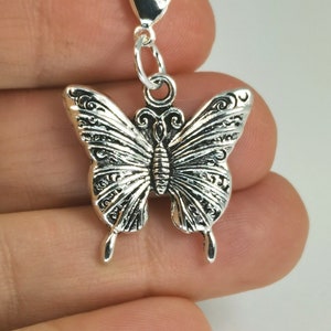 Può includere: Ciondolo a forma di farfalla argentato con un design dettagliato e un moschettone.
