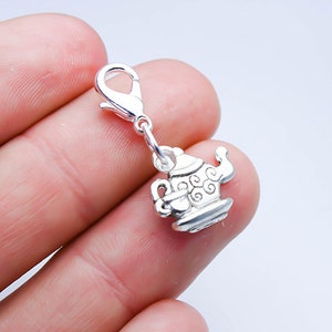 May include: Silver charm in the shape of a teapot with a swirl design. The charm has a lobster clasp.