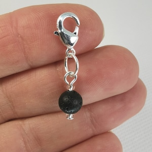 May include: A silver charm with a black lava rock bead and a silver lobster clasp.