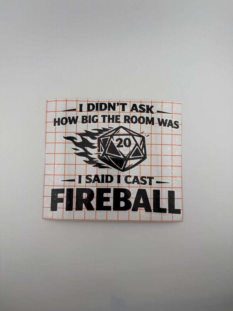 May include: A square sticker with a grid pattern and black text that reads "I DIDN'T ASK HOW BIG THE ROOM WAS. I SAID I CAST FIREBALL." A black and white die with the number 20 is in the center, with flames.