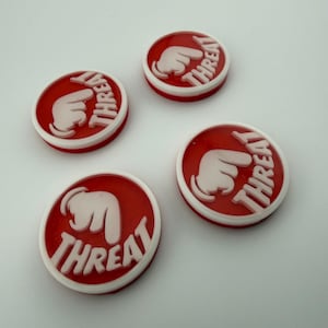 Peut inclure: Quatre boutons circulaires rouges et blancs avec le mot "THREAT" et un graphisme de doigt pointant. Les boutons ont une bordure blanche et sont disposés sur une surface blanche.