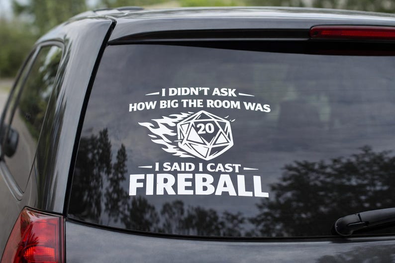 May include: A white vinyl decal on a car window. The decal features the text "I DIDN'T ASK HOW BIG THE ROOM WAS - I SAID I CAST FIREBALL" with a stylized D20 die graphic. The car is dark grey.