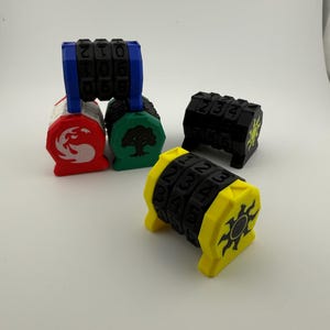 Puede incluir: Una colección de contadores de dados impresos en 3D y coloridos. Los contadores son de varios colores, incluyendo azul, rojo, verde, negro y amarillo. Cada contador presenta un dial giratorio con números y un símbolo único. Los contadores de dados están diseñados para juegos de mesa.