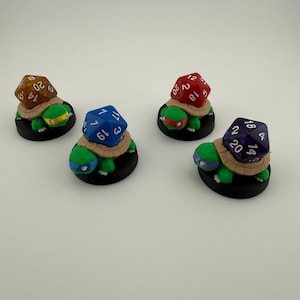 Può includere: Quattro miniature di tartarughe, ognuna con un dado di colore diverso sul dorso. I dadi sono marroni, blu, rossi e viola, con numeri bianchi. Le tartarughe sono verdi con basi nere e fasce colorate.