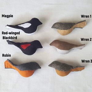 May include: Six felt bird ornaments, including a black and white magpie, a black red-winged blackbird, a brown wren, a gray and brown wren, a gray and brown wren, and a gray and orange robin.