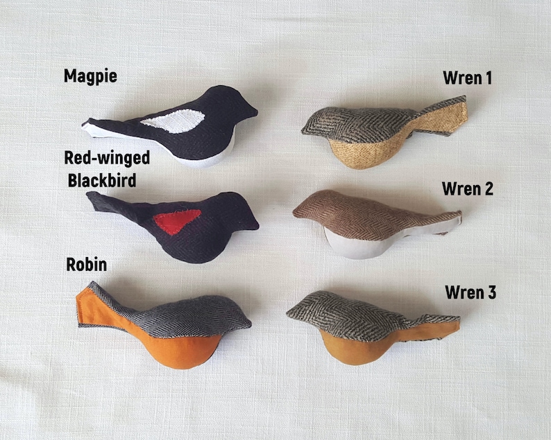 May include: Six felt bird ornaments, including a black and white magpie, a black red-winged blackbird, a brown wren, a gray and brown wren, a gray and brown wren, and a gray and orange robin.